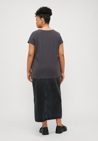 Gray short-sleeve t-shirt with a rounded neckline, paired with a long black denim skirt. Model wears black slip-on shoes. Simple design.