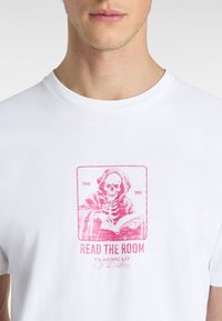 Hvid bomulds T-shirt med et pink grafisk print af et skelet, der læser en bog, samt teksten "READ THE ROOM" og branddetaljer.