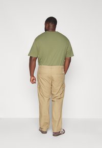 Groene katoenen T-shirt gecombineerd met lichte kaki cargobroek met zijzakken. De outfit heeft een relaxte pasvorm en een eenvoudig ontwerp.