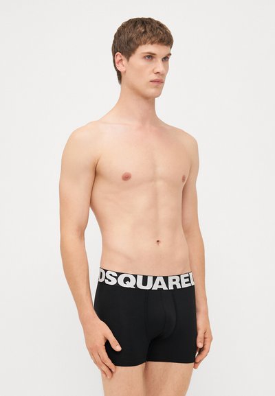 Černé boxerky s bílým logem "DSQUARED2" na pase, vyrobené z bavlny, těsného střihu a hladkého materiálu, nošeny modelem.