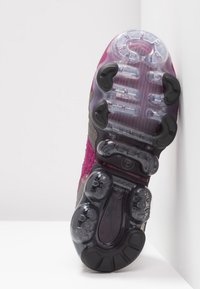Semelle d'une chaussure de sport rose et grise avec des sections en caoutchouc transparentes et noires avec coussin d'air sur fond blanc.