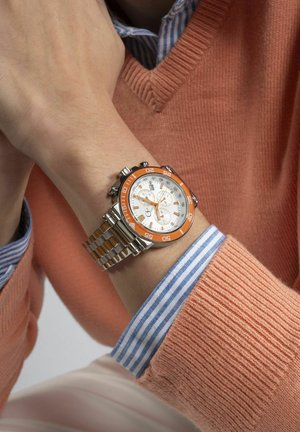 Sølv- og orange kvartsglasur med rund urskive, chronograf underdials og metal link-armbånd, båret på en hånd med struktureret stof under.