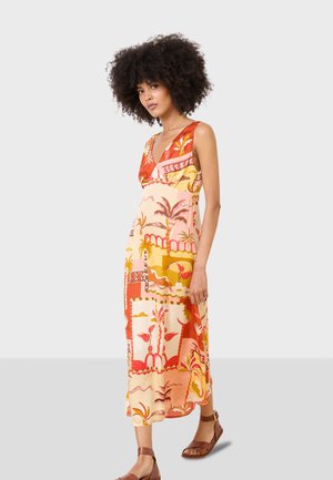 Bedrucktes Midi-Kleid mit V-Ausschnitt, lebhaften Mustern in Rot und Gelb sowie einem lockeren Schnitt mit fließender Textur. Braune Sandalen runden den Look ab.