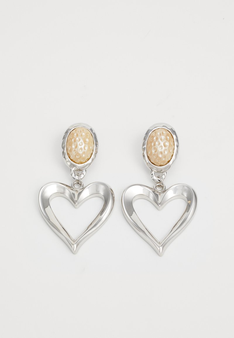 Zilveren hartvormige oorbellen met een glanzende afwerking. Elke oorbel heeft een gestructureerde beige ovale stud. Elegant en lichtgewicht ontwerp.