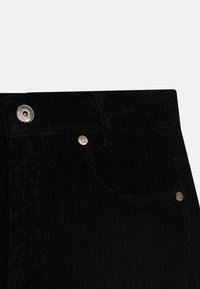 Pantaloni in corduroy neri che presentano una superficie testurizzata, cuciture visibili, una tasca frontale e dettagli in metallo argentato sulla vita.