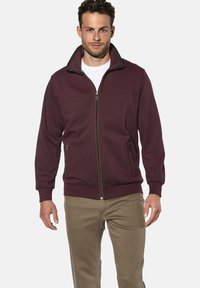 Burgunderfarbene Zip-Hoodie mit hohem Kragen, zwei seitlichen Taschen und gerippten Bündchen. Hergestellt aus weichem Stoff mit glatter Textur.