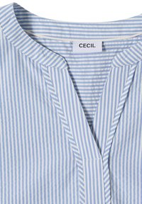 Col et encolure d'une chemise rayée verticalement bleu et blanc avec un petit col en V et une étiquette de marque "CECIL" à l'intérieur.