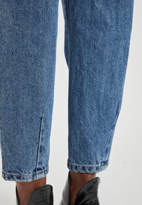 Jasnoniebieskie dżinsy o luźnym kroju, widoczne detale szwów oraz podwinięte mankiety, w połączeniu z czarnymi, wypolerowanymi butami.