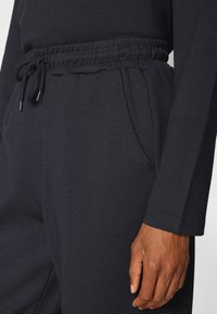 Zwarte trainingsbroek met een elastische tailleband en een trekkoord, zijzakken en een gladde, ademende stof.