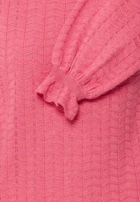 Tissu tricoté rose avec un motif zigzag texturé et un poignet froncé sur une manche longue.
