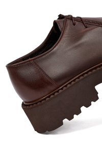 Scarpa in pelle marrone con punta arrotondata, superficie texturizzata e suola in gomma marrone spessa e robusta con motivo a zigzag.