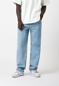 Lichtblauwe denim jeans met een relaxte pasvorm en rechte pijpen, gecombineerd met een wit T-shirt en grijze/zilveren sneakers. Minimalistische stijl.