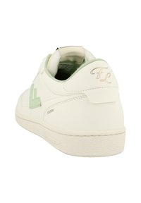 Scarpa da ginnastica bianca con accenti verde chiaro, scritta in oro "FL" sul tallone e "Stadion" stampato sul lato vicino alla suola, vista dal retro a sinistra.