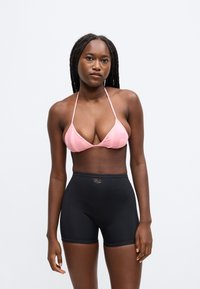 Ružový trojuholníkový plavkový top s tenkými ramienkami, kombinovaný s čiernymi vysoko pásovými šortkami. Materiál je hladký a elastický.