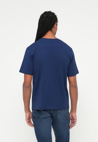 Mornaricna modra majica iz bombaža s kratkimi rokavi, okroglim ovratnikom in ravnim robom, oblečena z denim hlačami.