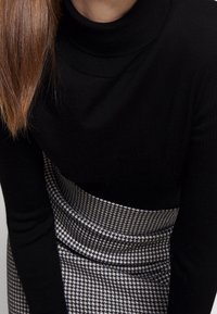 Un pull noir à col roulé associé à une jupe à motif pied-de-poule, présentant une coupe ajustée et une texture côtelée au niveau du col et des poignets.