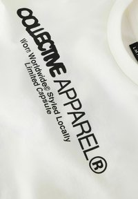 Hvit bomulls-t-skjorte med fet svart tekst: "COLLECTIVE APPAREL® Worn Worldwide® Styled Locally Limited Capsule" med en myk tekstur.