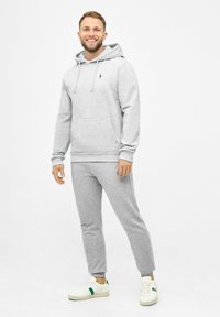 Felpa con cappuccio grigio chiaro e pantaloni jogger abbinati realizzati in tessuto morbido, dotati di una tasca frontale e un piccolo emblema sul petto.