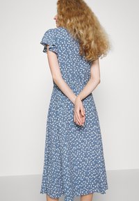 Blå blommig klänning med korta volanger på ärmarna, med en knälång kjol och lätt tyg. Små vita blommor över hela.