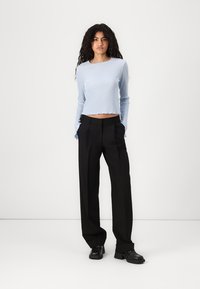 Hellblau gestreiftes langärmliges Crop-Top kombiniert mit schwarzen weit geschnittenen Hosen und schwarzen klobigen Schuhen. Einfaches Design mit minimalen Akzenten.