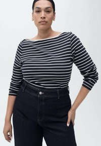 Marineblauwe en witte gestreepte longsleeve top met een bootnek, gecombineerd met hoogopgemerkte donkere denim jeans met een zilveren knoop en stikdetails.