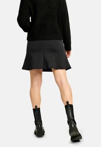 Černá rozšířená sukně s bílými puntíky, vyrobená z hladké látky. Kombinována s černým texturovaným svetrem a masivními černými botami.