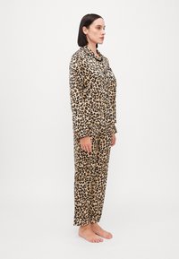 Pajama set s uzorkom leoparda od mekog materijala; majica s dugim rukavima i detaljima na dugmadima te odgovarajuće široke hlače. Lagani i šareni dizajn.