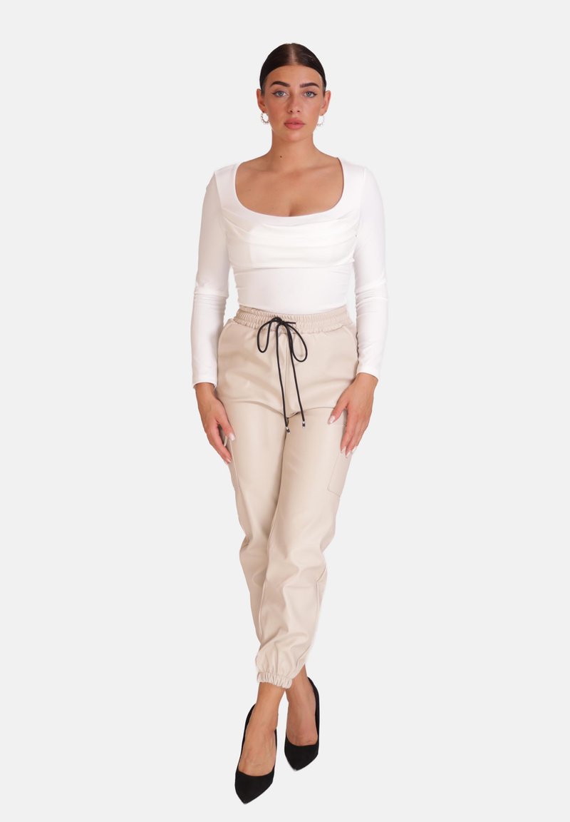 Beige Joggings aus Kunstleder mit elastischen Bündchen und elastischem Bund, kombiniert mit einem eng anliegenden weißen Langarmshirt und schwarzen High Heels.