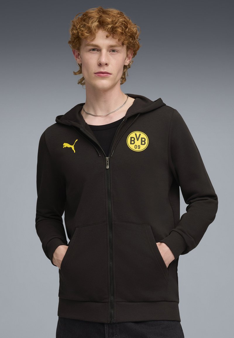 Crna zip-up dukserica izrađena od mekanog materijala, s kengurujem džepom, rebrastim manžetama i žutim okruglim logotipom s natpisom "BVB 09" na prsima.