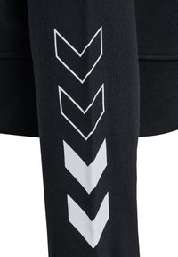 Sweatshirt noir avec un motif en chevrons blancs sur la manche, fabriqué à partir d'un tissu texturé, mettant en valeur une silhouette ajustée et des lignes épurées.