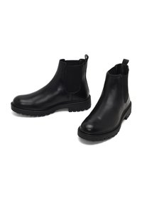 Bottines Chelsea en cuir noir avec panneaux élastiques sur les côtés, bout arrondi et semelle en caoutchouc texturé. Comprend une poignée pour un enfilage facile.