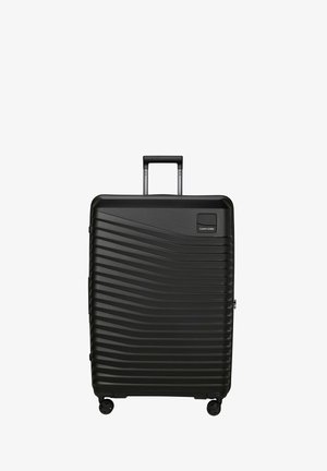 Valise rigide noire à motif ondulé horizontal, équipée de quatre roues et d'une poignée extensible, marque Samsonite.