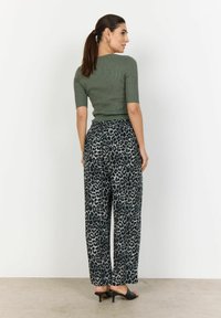 Olive green ribbed top, leopard print wide-leg trousers, and black heeled mules. Smooth textile with a relaxed fit and contrasting patterns.