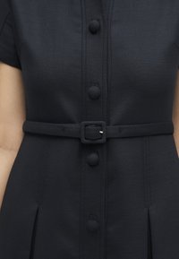 Μαύρο φόρεμα με κουμπιά καλυμμένα με ύφασμα και ταιριαστή ζώνη με τετράγωνη αγκράφα στη μέση.