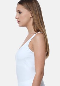 White sleeveless top with a v-neck design, featuring a smooth texture and fitted silhouette, shown from the side against a neutral background.