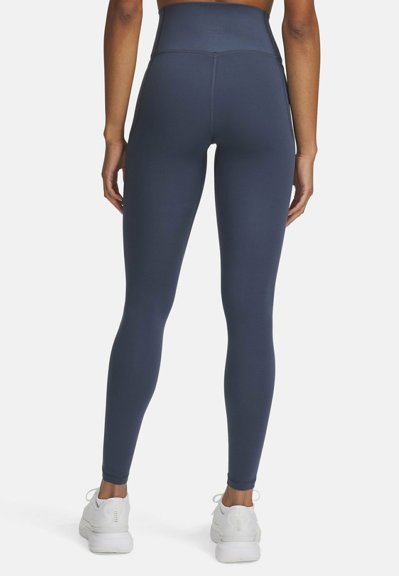 Leggings atletici a vita alta di colore blu navy, realizzati in tessuto elastico, caratterizzati da una texture liscia e un design aderente, abbinati a sneaker bianche.