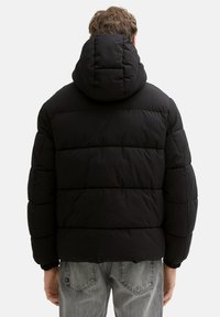 Musta toppatakki irrotettavalla hupulla, sisältää tikatun kuvion, joustavat hihansuut ja sileän pinnan. Ei näkyviä logoja tai korostuksia.