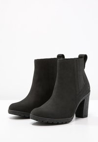 Bottines en cuir suédé noir avec un talon bloc texturé et des panneaux latéraux élastiques. Extérieur lisse avec des tirants pour un enfilage facile.
