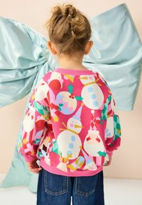 Helles pinkes Sweatshirt mit festlichen Schneemännern, dem Weihnachtsmann und Weihnachtsmustern. Lange Ärmel mit gerippten Bündchen und Saum. Lässige Passform.