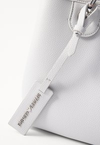 Biała torebka ze skóry o fakturze, z prostokątną metką z wytłoczonym napisem marki „EMPORIO ARMANI” oraz srebrnym elementem ozdobnym.