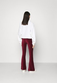Vit oversize sweatshirt med sänkta axlar, kombinerad med bordeauxvelour byxor med vida ben. Modellen står framför en enfärgad bakgrund.