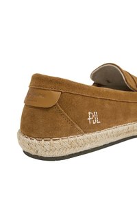 Scarpa slip-on in suede marrone con suola in corda di juta, accento in pelle sul tallone e iniziali ricamate bianche "PJL" sul lato.