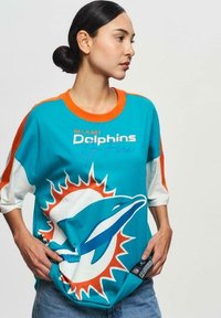 Miami Dolphins t-shirt, teal med oranga accenter, har en delfinlogotyp och text. Lässig passform, tre-kvarts ärmar, blandmaterial av bomull.
