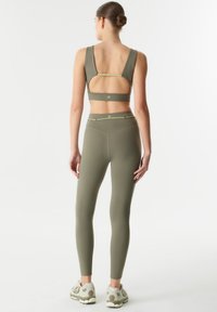 Soutien-gorge de sport vert à dos ouvert, associé à un legging taille haute assorti. Tissu lisse, coutures minimales et accents élastiques.