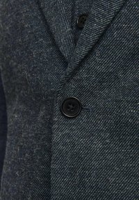Texturiertes dunkelblaues Wollblazer mit einem Reverskragen, zwei schwarzen Knöpfen und einem diagonalen Webmuster.