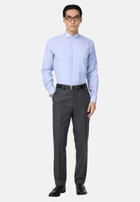 Šviesiai mėlynas dryžuotas marškinių švarkas, pritaikytas pagal figūrą, derinama su tamsiai pilkais plokščiais kelnais. Juodi odiniai batai ir diržas užbaigia aprangą.