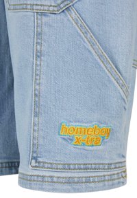 Gaiši zili džinsu šorti ar dzelteniem šuvumiem un daudzkrāsainu izšūtu logo "homeboy x-tra" sānos.