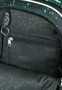 Zaino nero con un motivo digitale verde a binario. Presenta una tasca frontale con zip, tessuto testurizzato e un accento in metallo circolare.