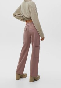 Pantalon de survêtement ample rose avec poches latérales et arrière, doté d'une ceinture confortable. Associé à un haut beige à manches longues et court.