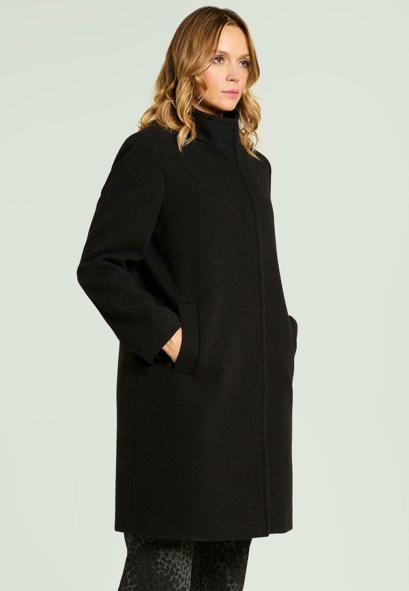 Abrigo negro con cuello alto, silueta recta y bolsillos ocultos. Presenta una textura suave y un diseño limpio, adecuado para diversas ocasiones.